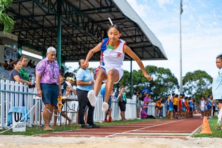 In full flight in the long jump as officials and spectators look on.